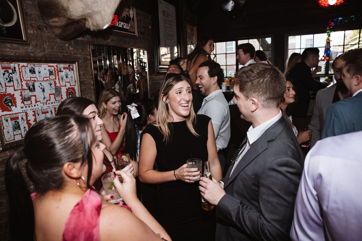Guests socializing and laughing at lively wedding reception party in rustic bar venue.