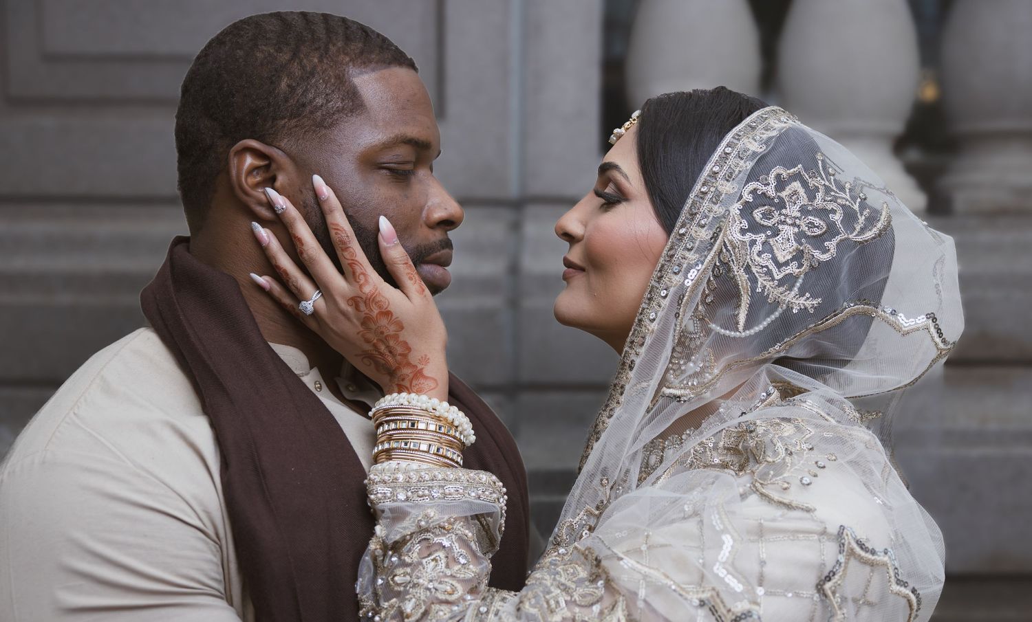Muslim bride in embroidered hijab and groom sharing tender moment at wedding ceremony.
