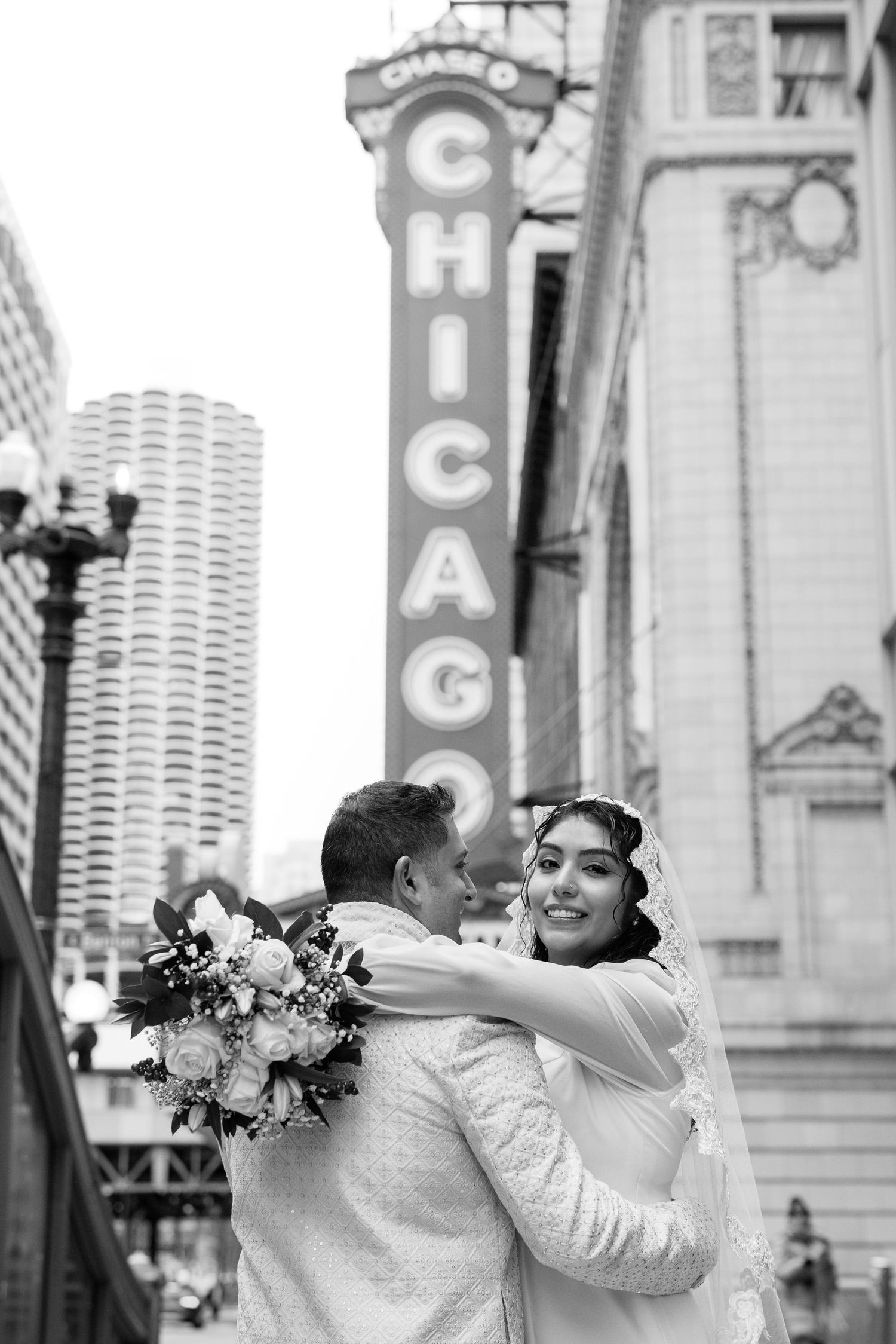 Black and white photo of bride and groom embracing in front of iconic Chicago Theatre sign.