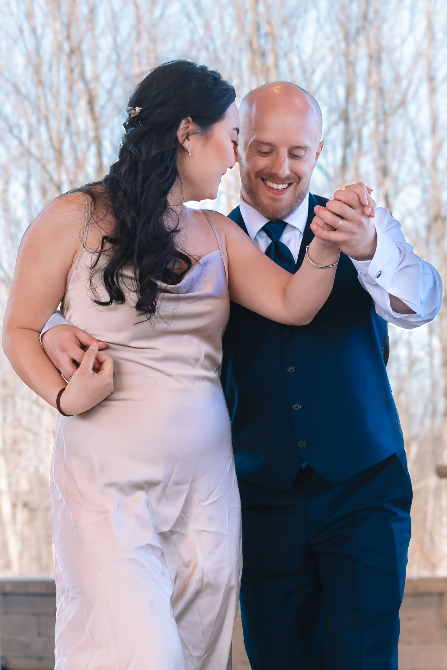 Groom in navy vest smiles joyfully while dancing with bride in blush gown at wedding reception.