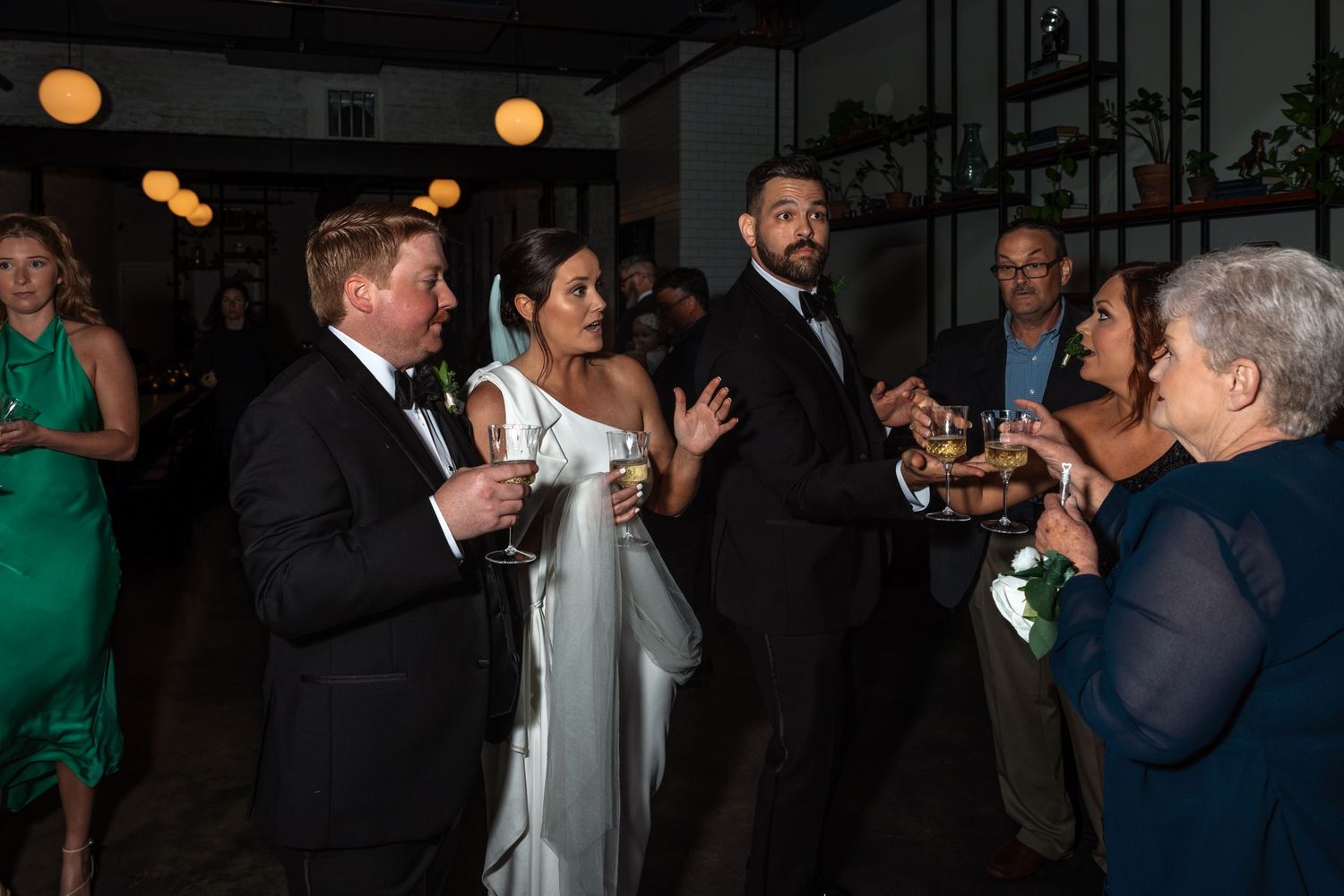 Wedding party guests mingle and chat animatedly at elegant indoor reception venue with warm ambient lighting.