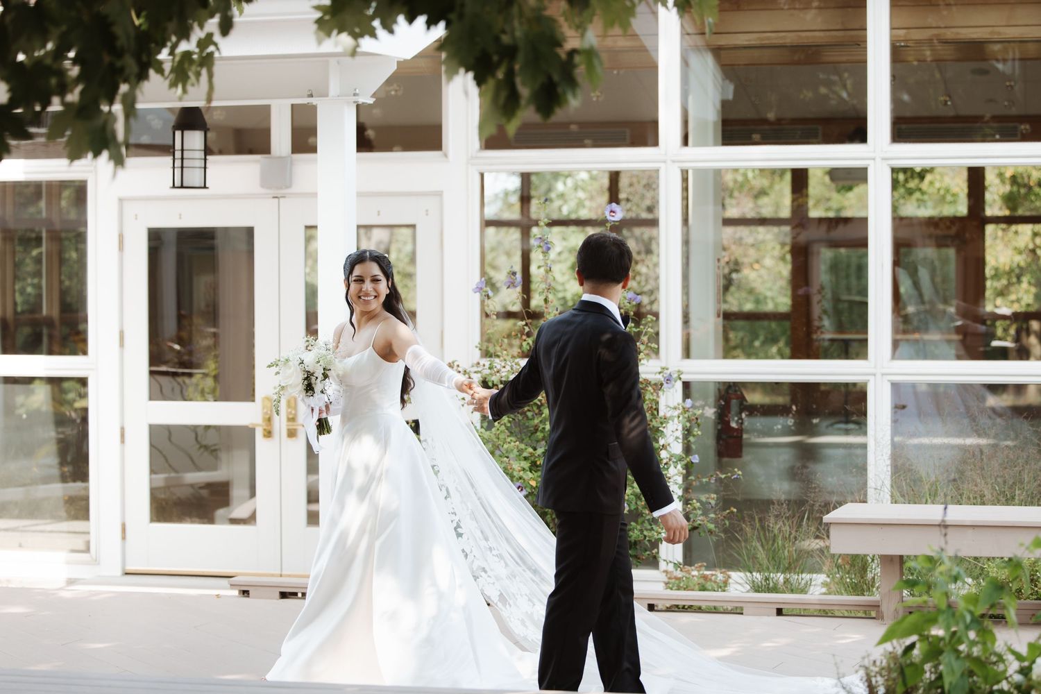 Bride and groom share first look moment outside a glass-windowed wedding venue.
