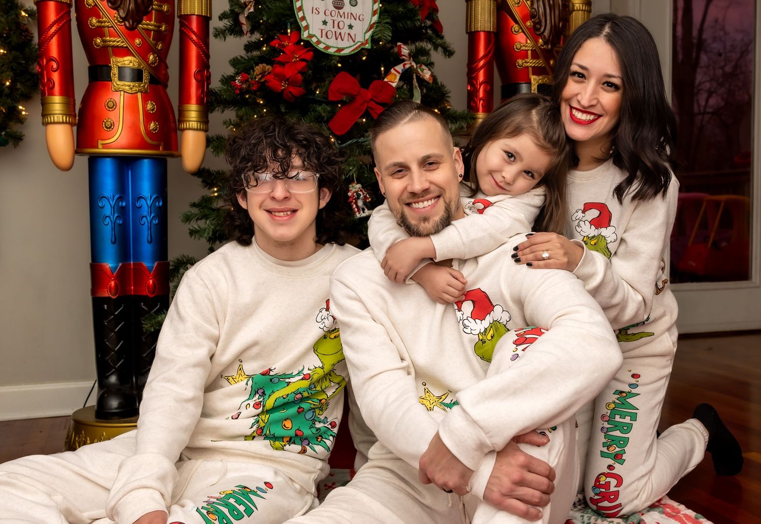 Cheerful family wearing matching white Grinch holiday pajamas smiling together near a Christmas tree.
