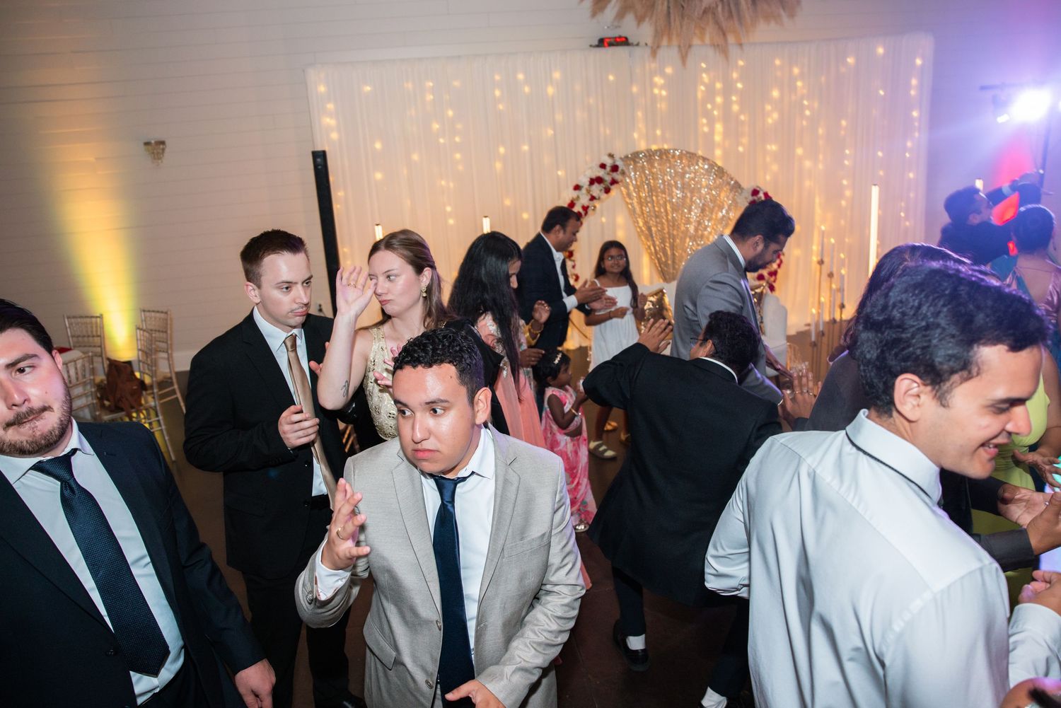 Guests dancing and celebrating at a lively wedding reception with fairy lights backdrop.
