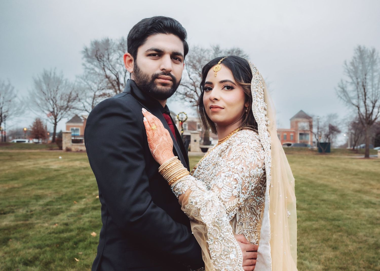 Pakistani bride and groom in intimate outdoor portrait, bride in gold embroidered lehenga.