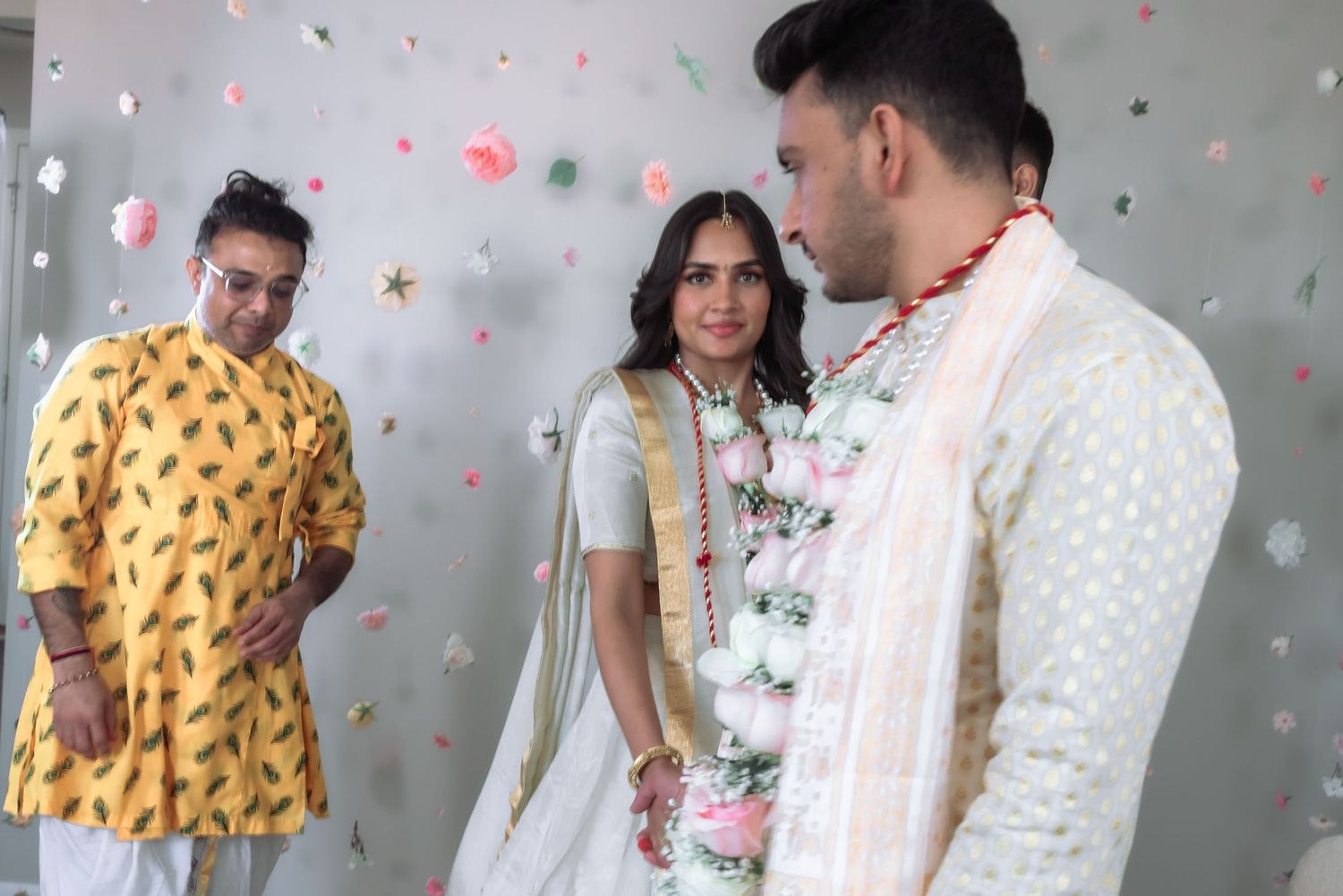 Indian wedding couple in traditional attire with family member in yellow kurta.