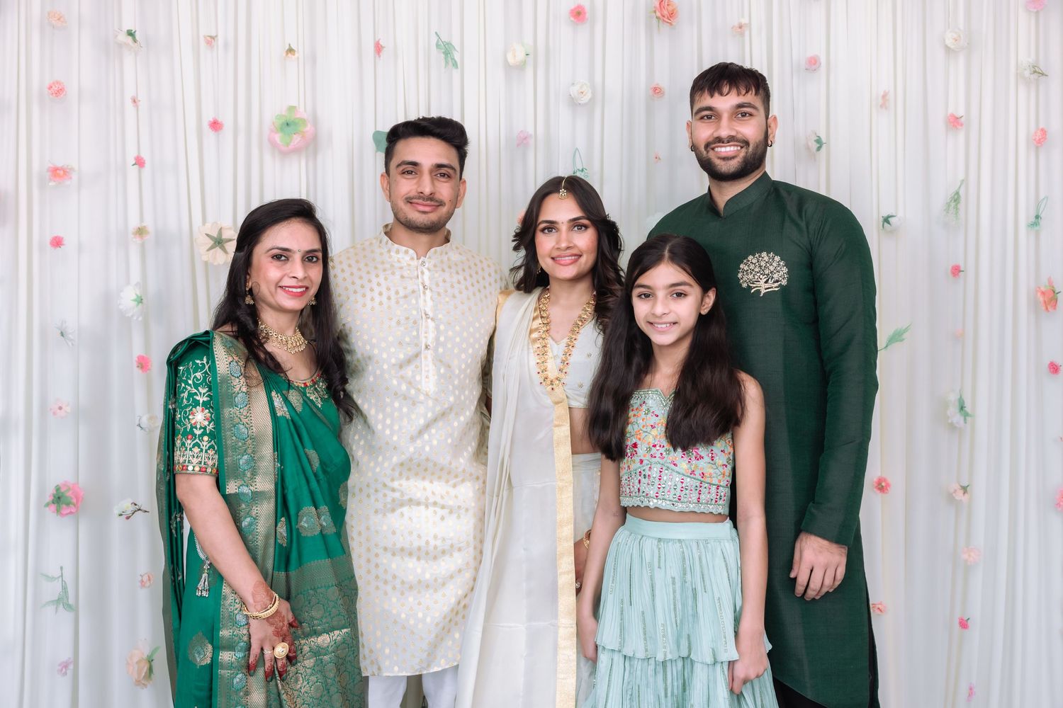 Group of five in traditional Indian attire including green and white outfits posing together at a festive event.