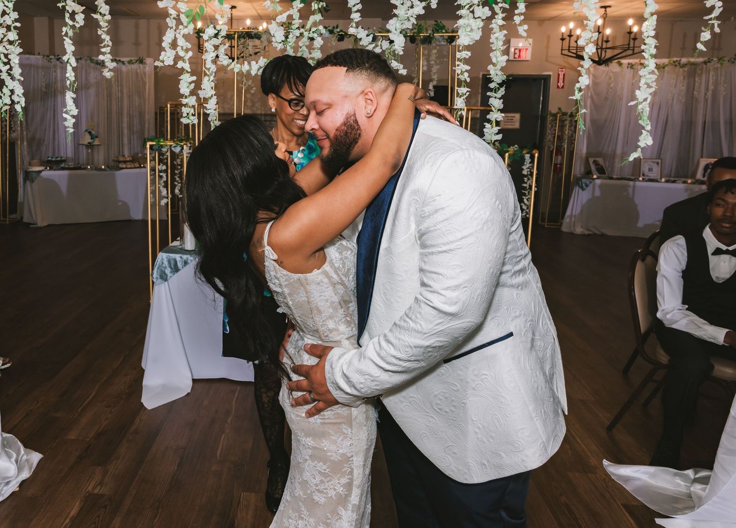 Bride and groom share romantic first kiss during wedding reception in beautifully decorated venue with hanging florals.