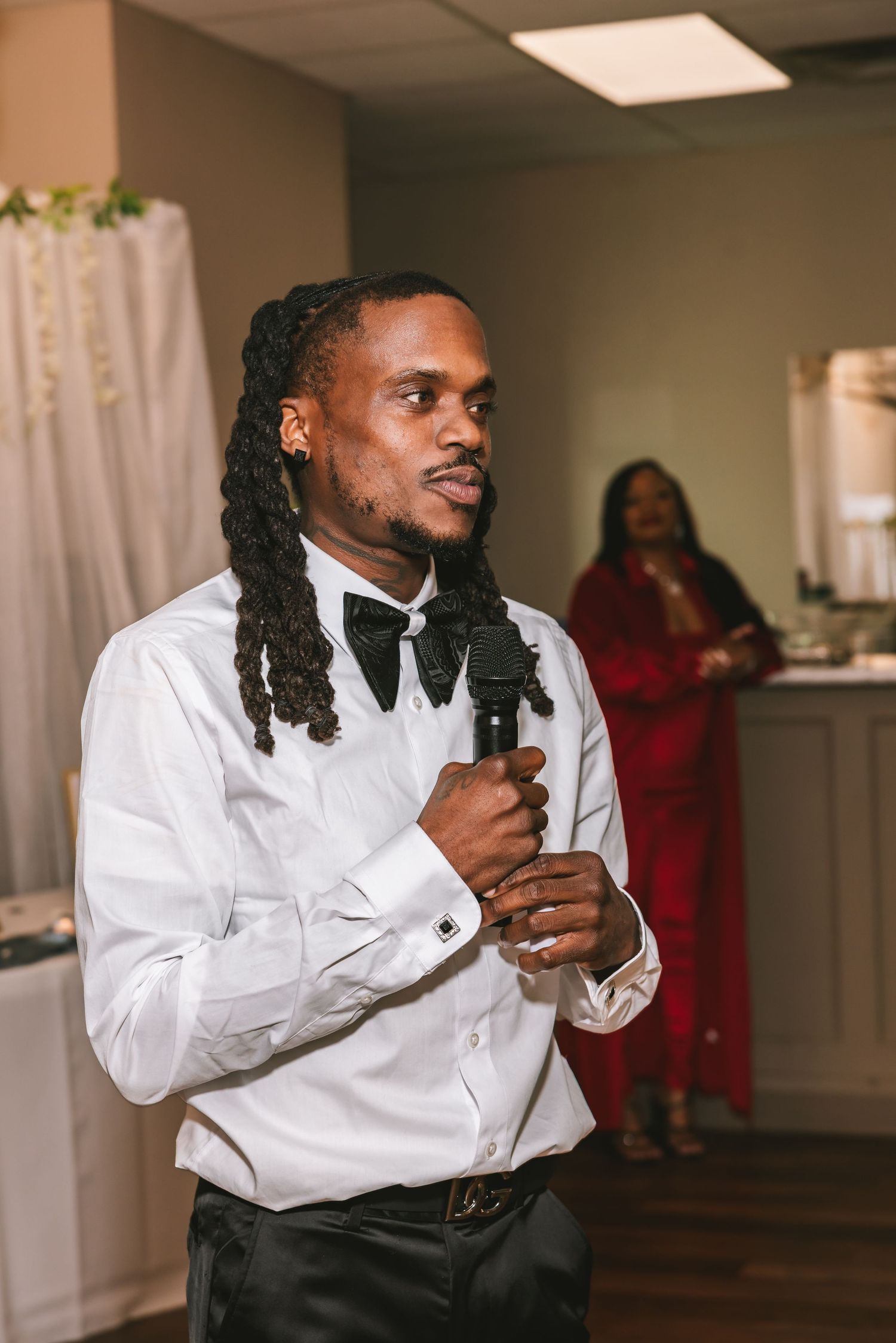 Man with dreadlocks in white shirt and bow tie gives a heartfelt speech at wedding reception.
