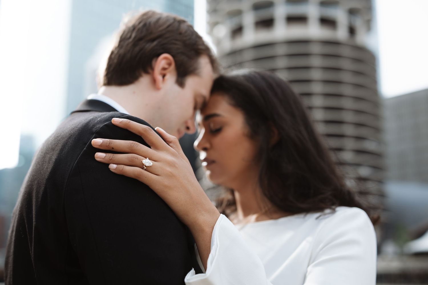 Couple sharing a tender moment with engagement ring visible against urban skyline backdrop.