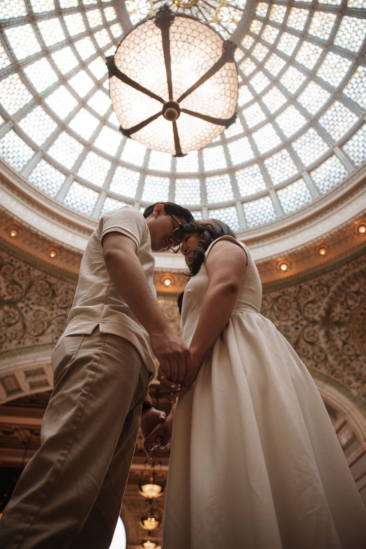 Low angle shot of couple holding hands beneath the breathtaking stained glass dome of the Chicago Cultural Center.