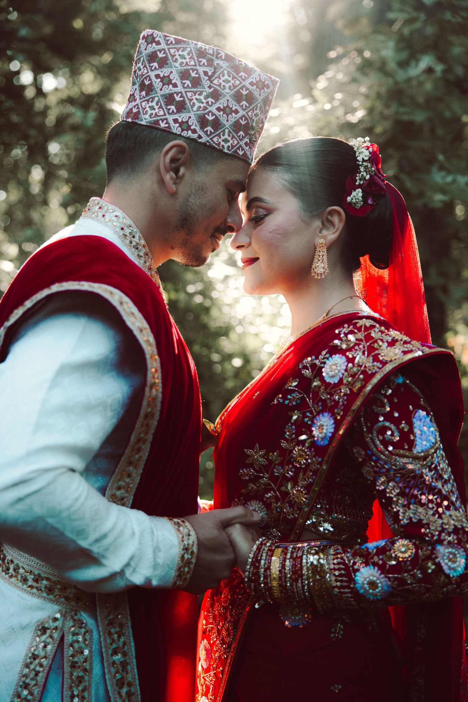 Couple in traditional Nepali wedding attire, groom in white and red, bride in embroidered red saree, sharing an intimate moment.