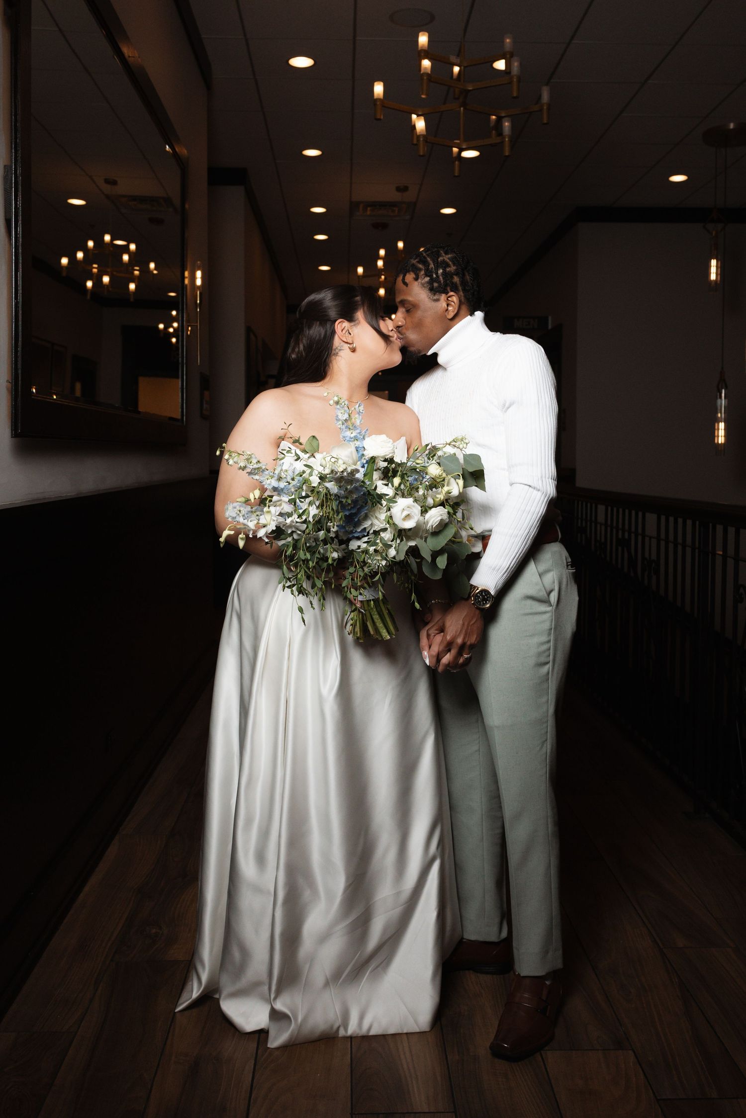 Bride and groom share intimate moment in elegant dark restaurant hallway, bride holding white bouquet.