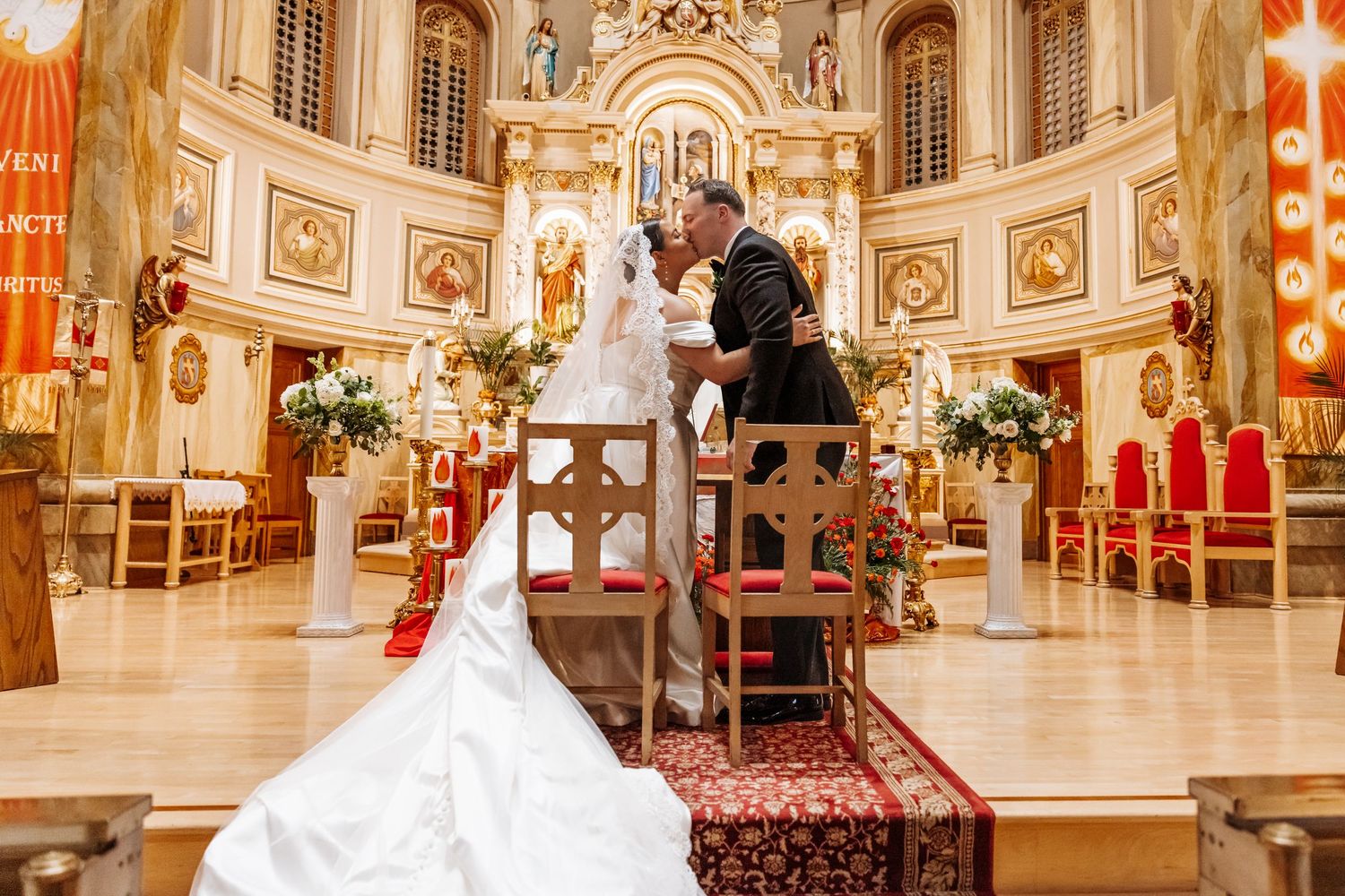 Bride and groom share a romantic kiss at the altar of an ornate Catholic church during their wedding ceremony.