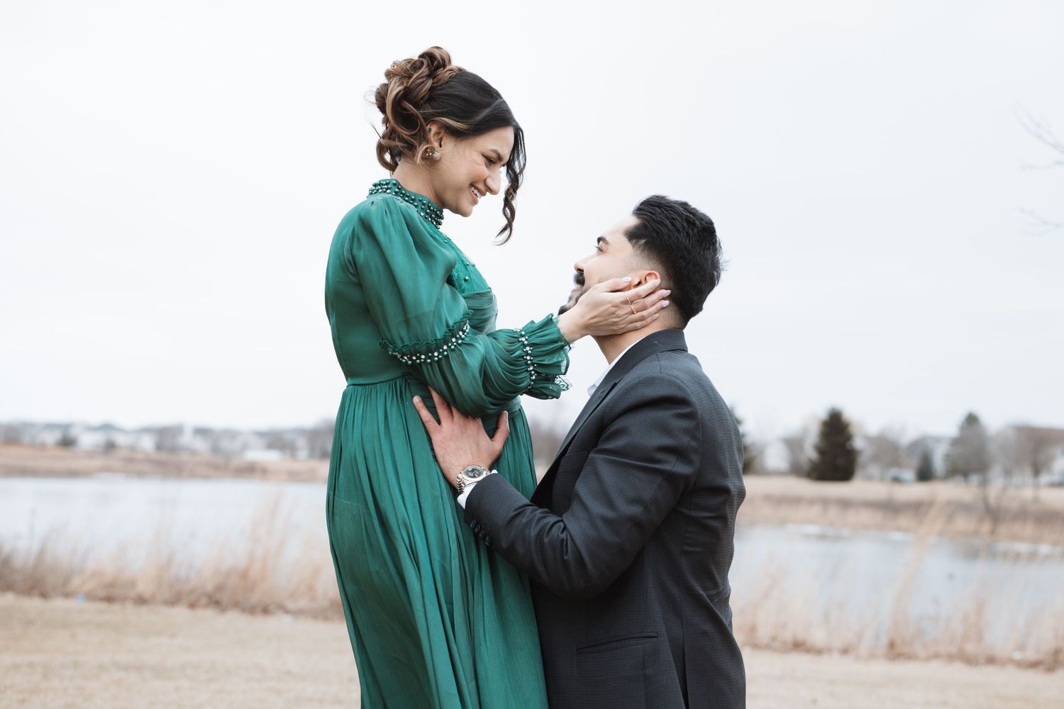 Pregnant woman in green dress laughing with bearded man during maternity photoshoot outdoors.