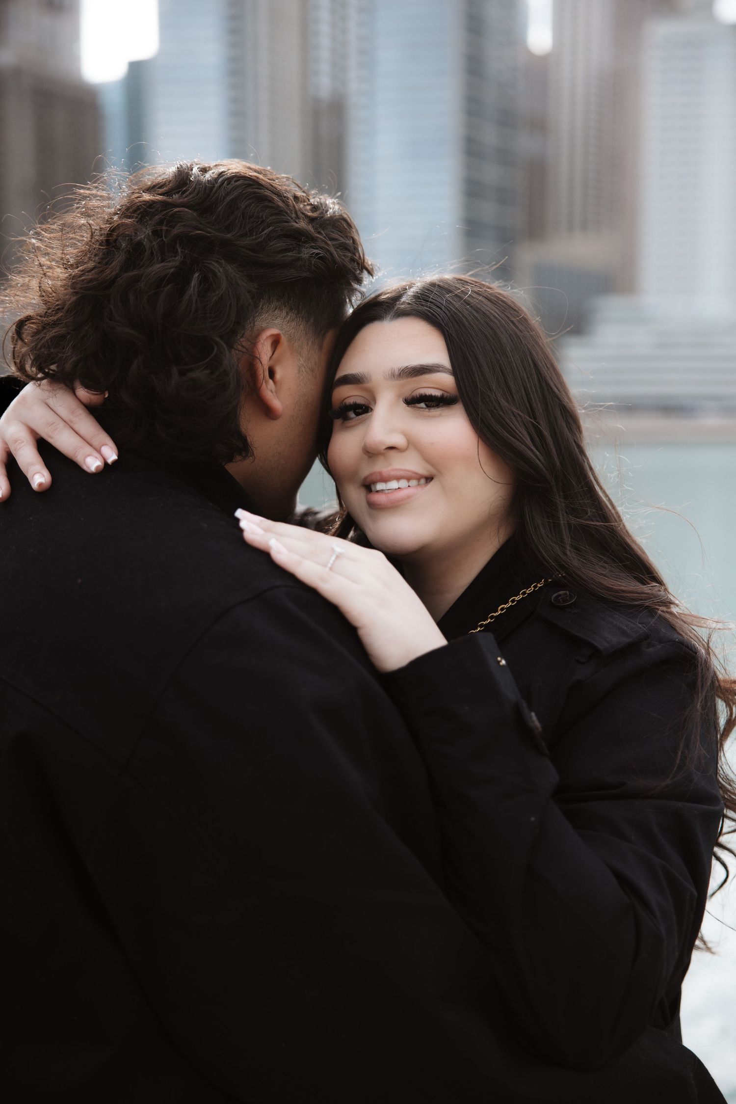 Smiling woman embraces partner near Chicago River with city buildings in background.