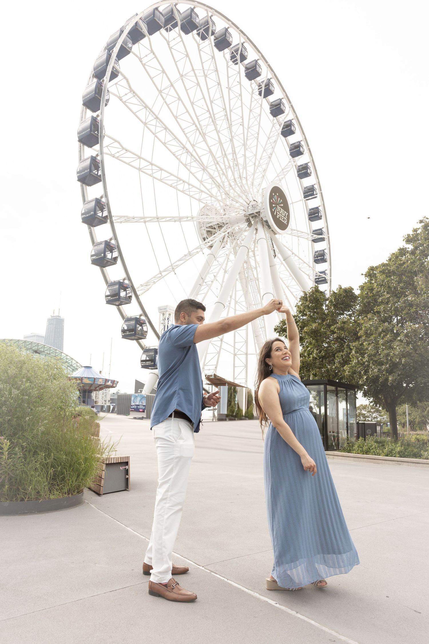 Couple dancing in front of a large Ferris wheel, woman in blue maxi dress being twirled by man in white pants.