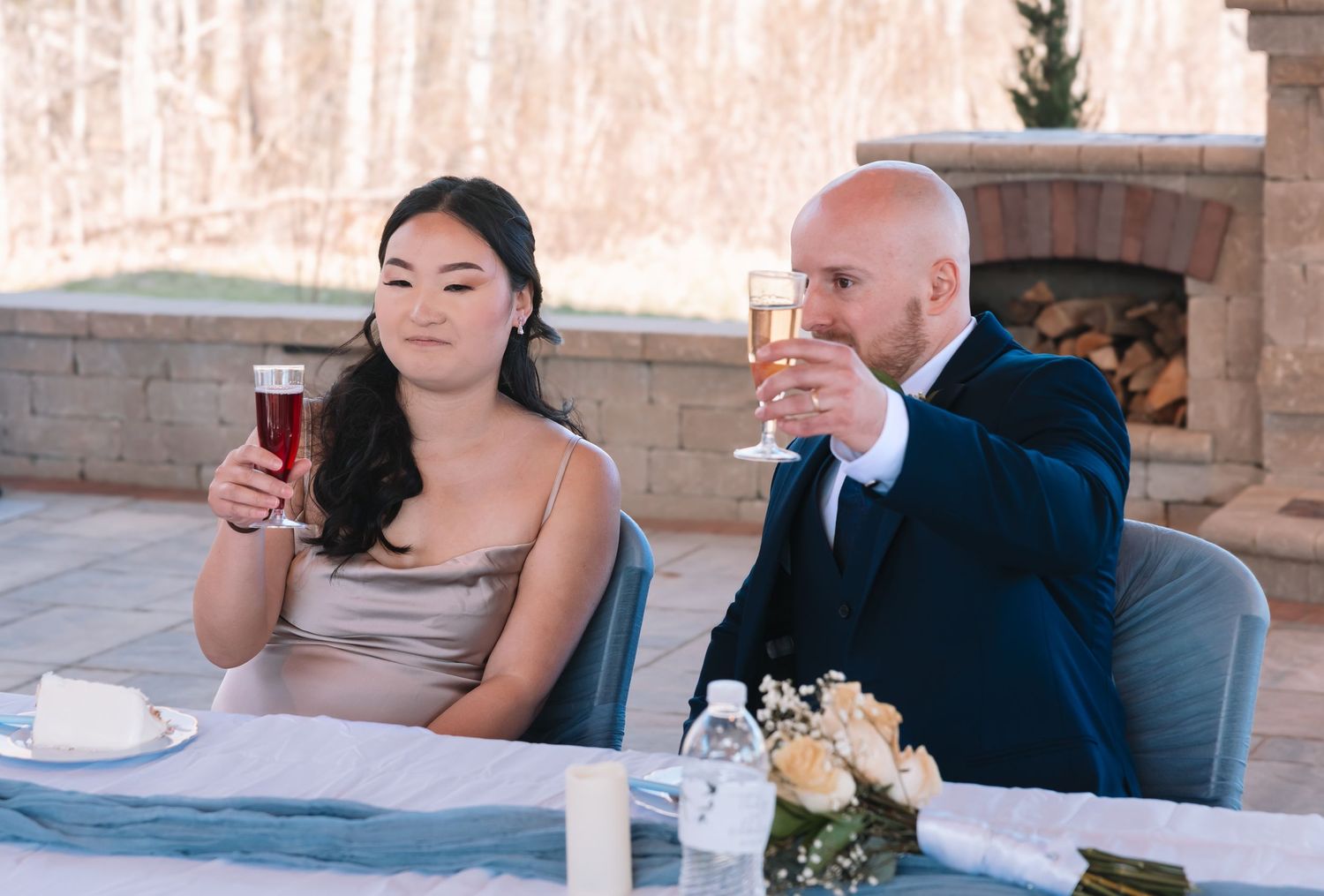 A bride and groom raise their glasses in a toast while seated at their wedding reception table.