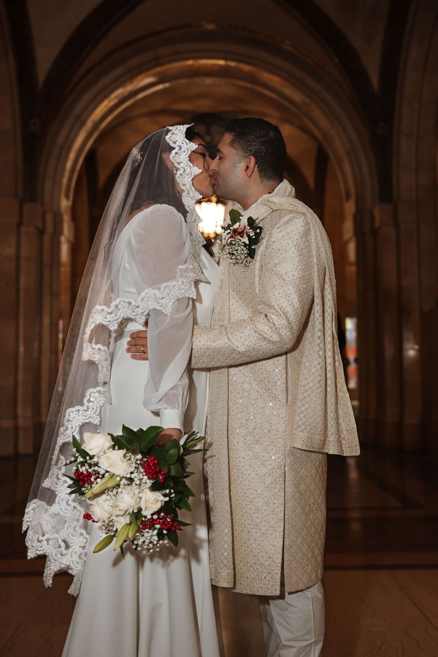Bride and groom sharing a kiss inside an ornate arched hallway on their wedding day.
