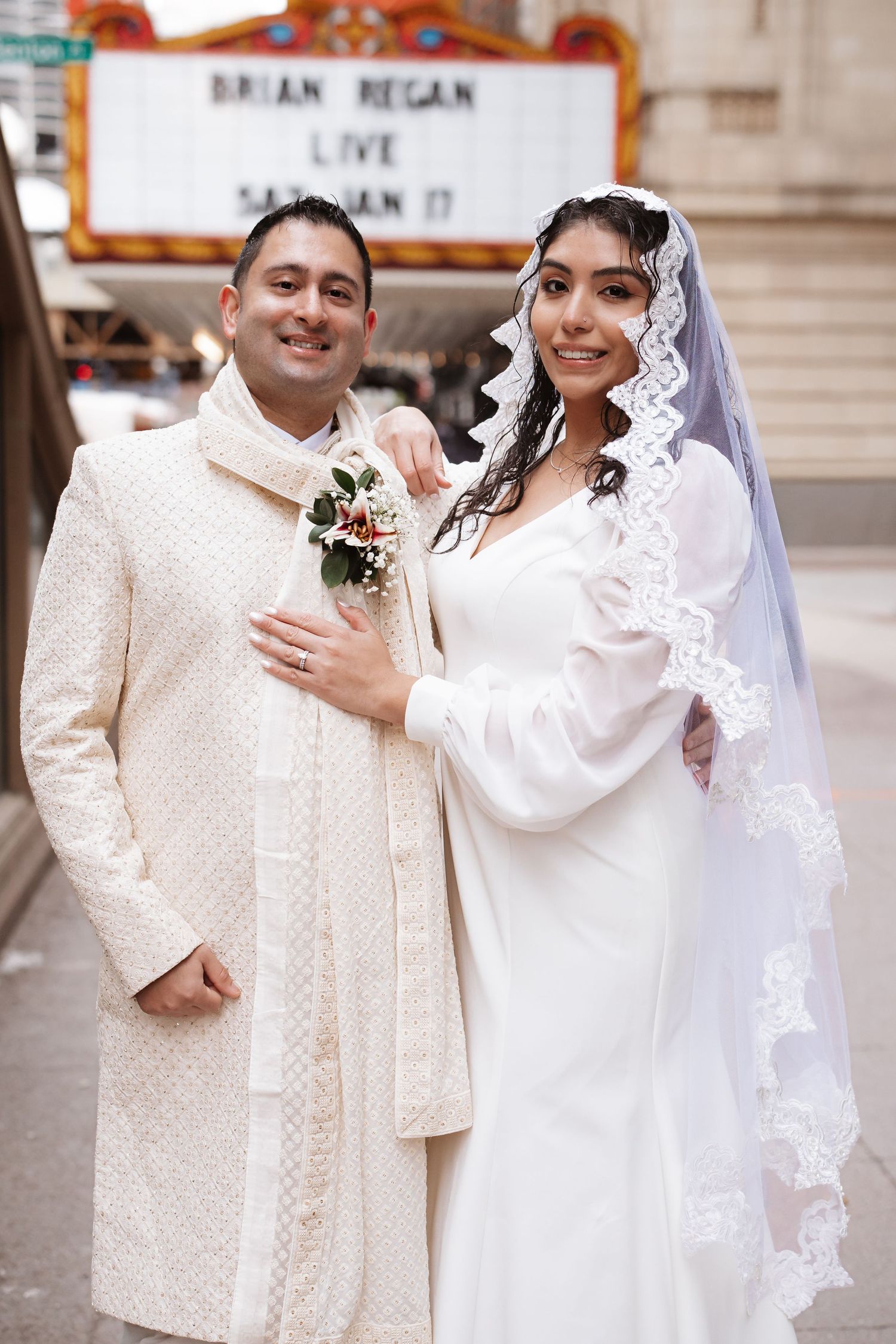 Smiling newlyweds pose together outside Chicago Theatre, bride holding floral bouquet in white gown.
