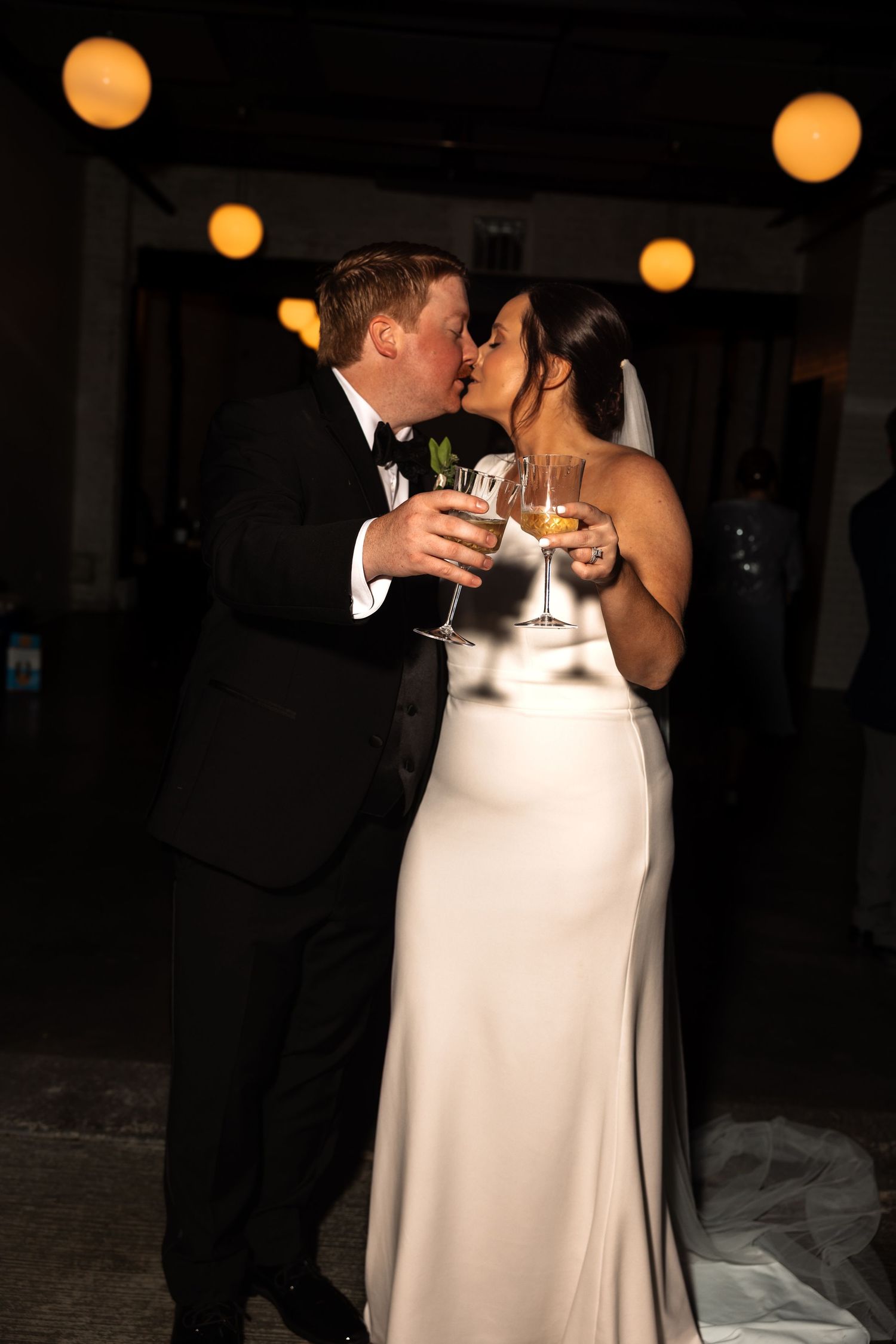 Newlyweds sharing a romantic kiss while holding champagne glasses at their reception.