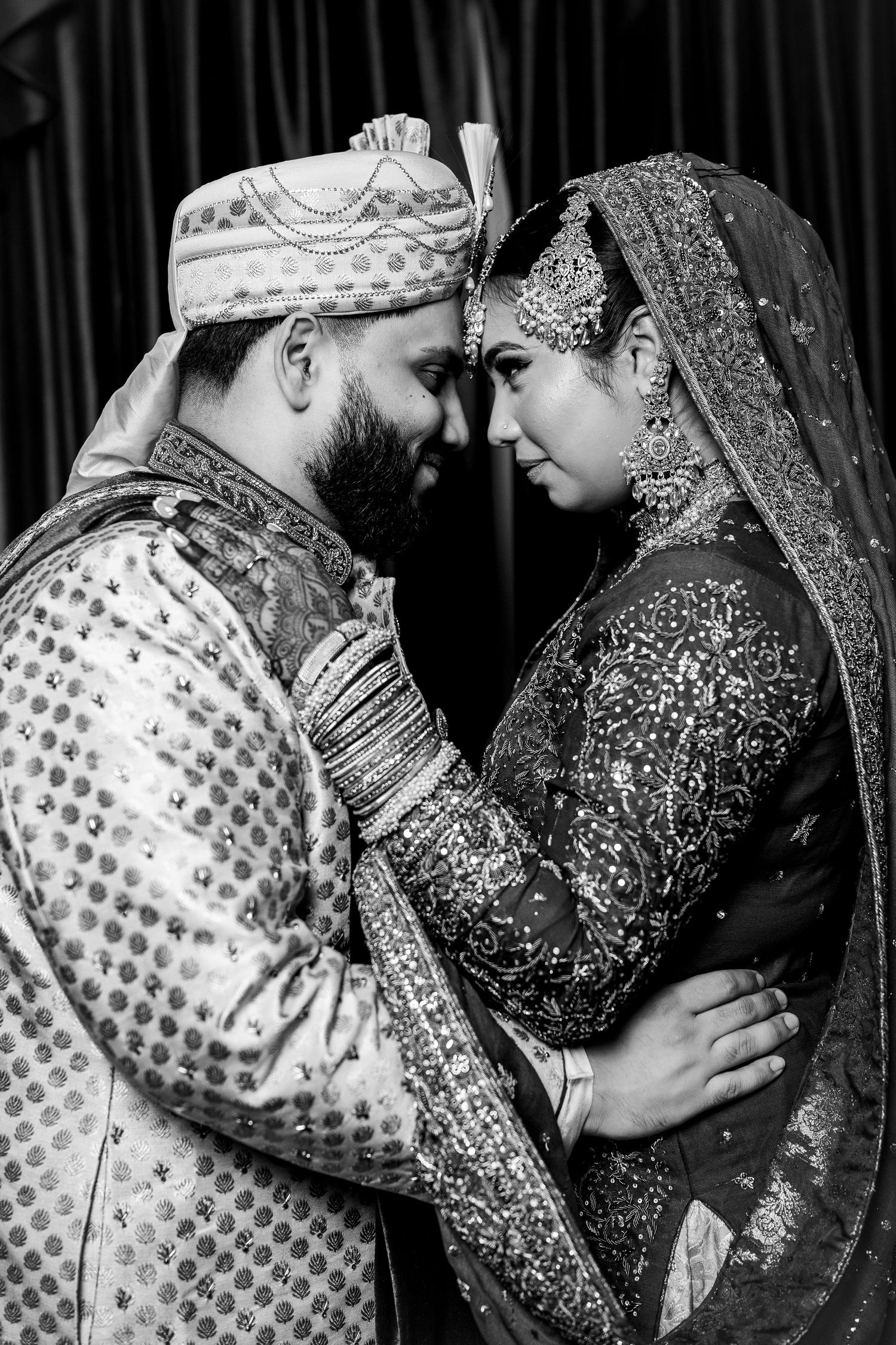 Black and white portrait of Indian bride and groom in traditional wedding attire touching foreheads.
