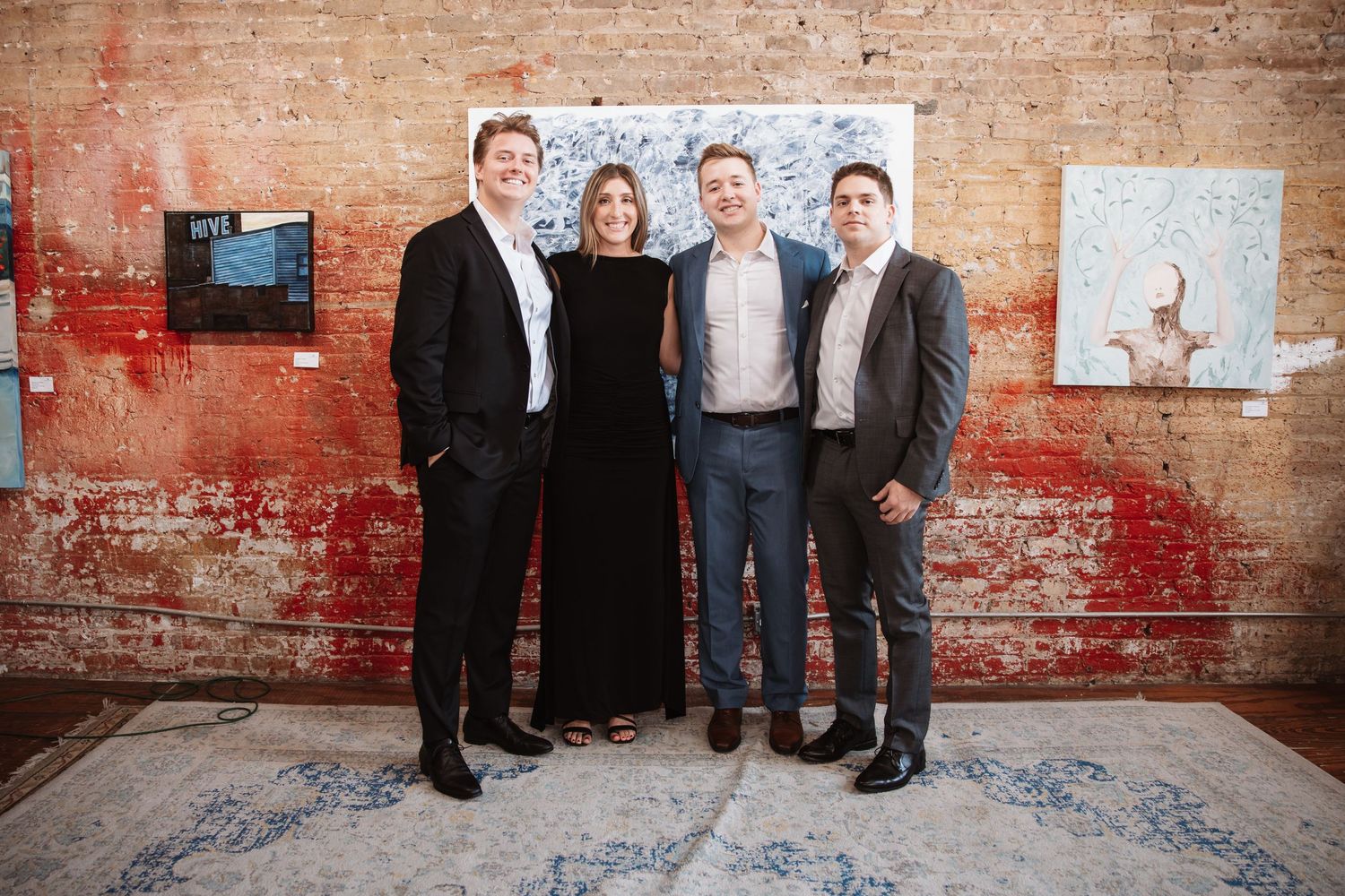 Four colleagues posing at an upscale art gallery networking event with brick wall background.