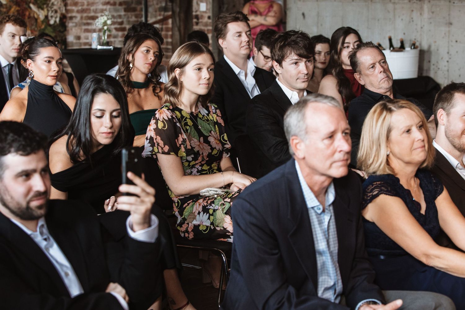 Wedding guests seated and engaged during indoor ceremony in brick venue.