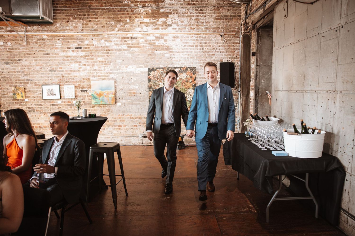 Two men in suits walking through a rustic brick-walled event venue with hardwood floors.