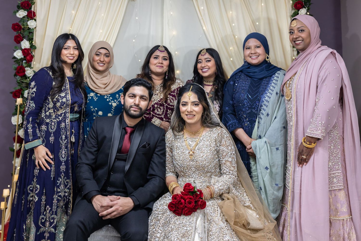 South Asian bride and groom with group of female guests at decorated wedding mandap.