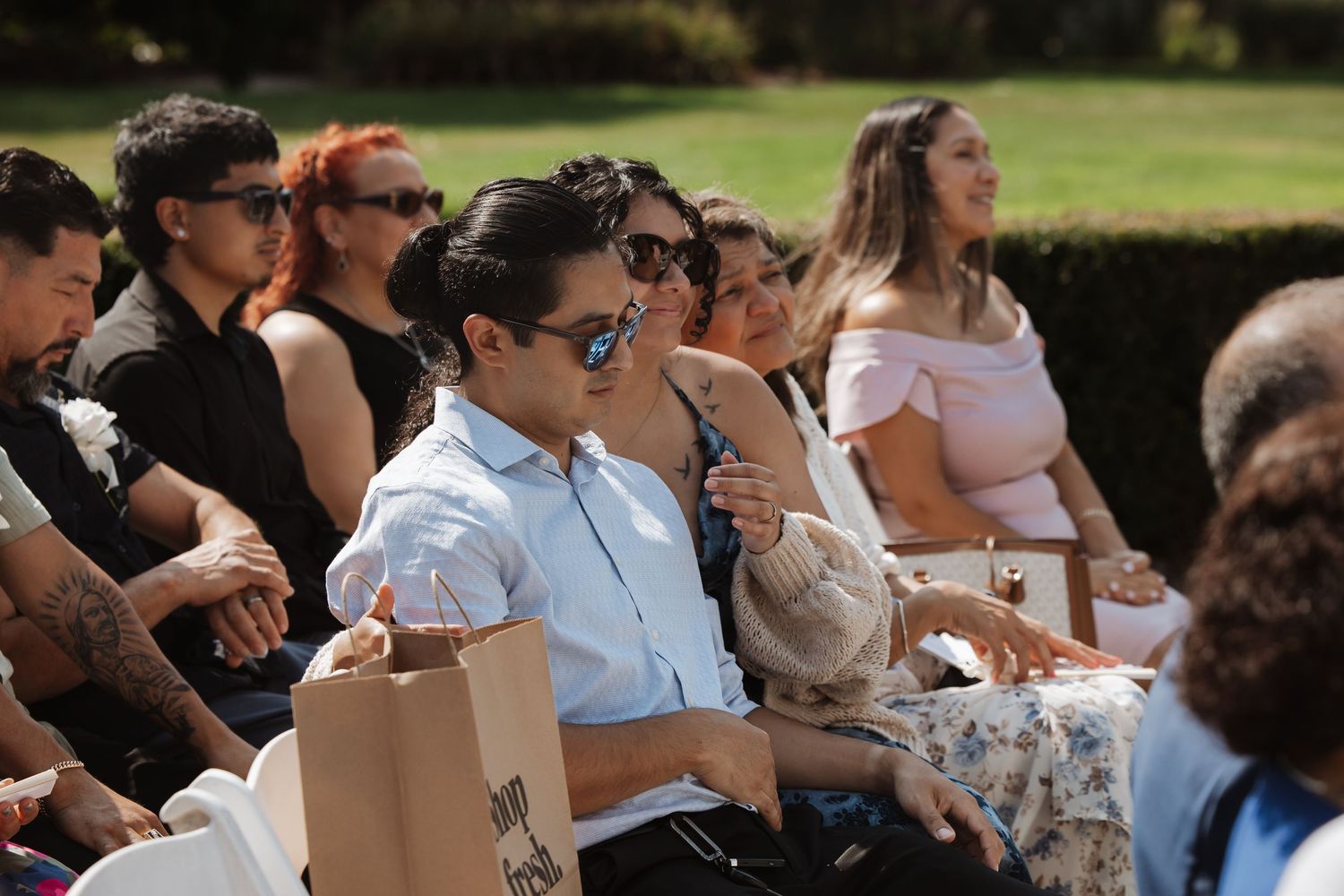 Wedding guests smile and laugh while seated at sunny outdoor wedding ceremony.