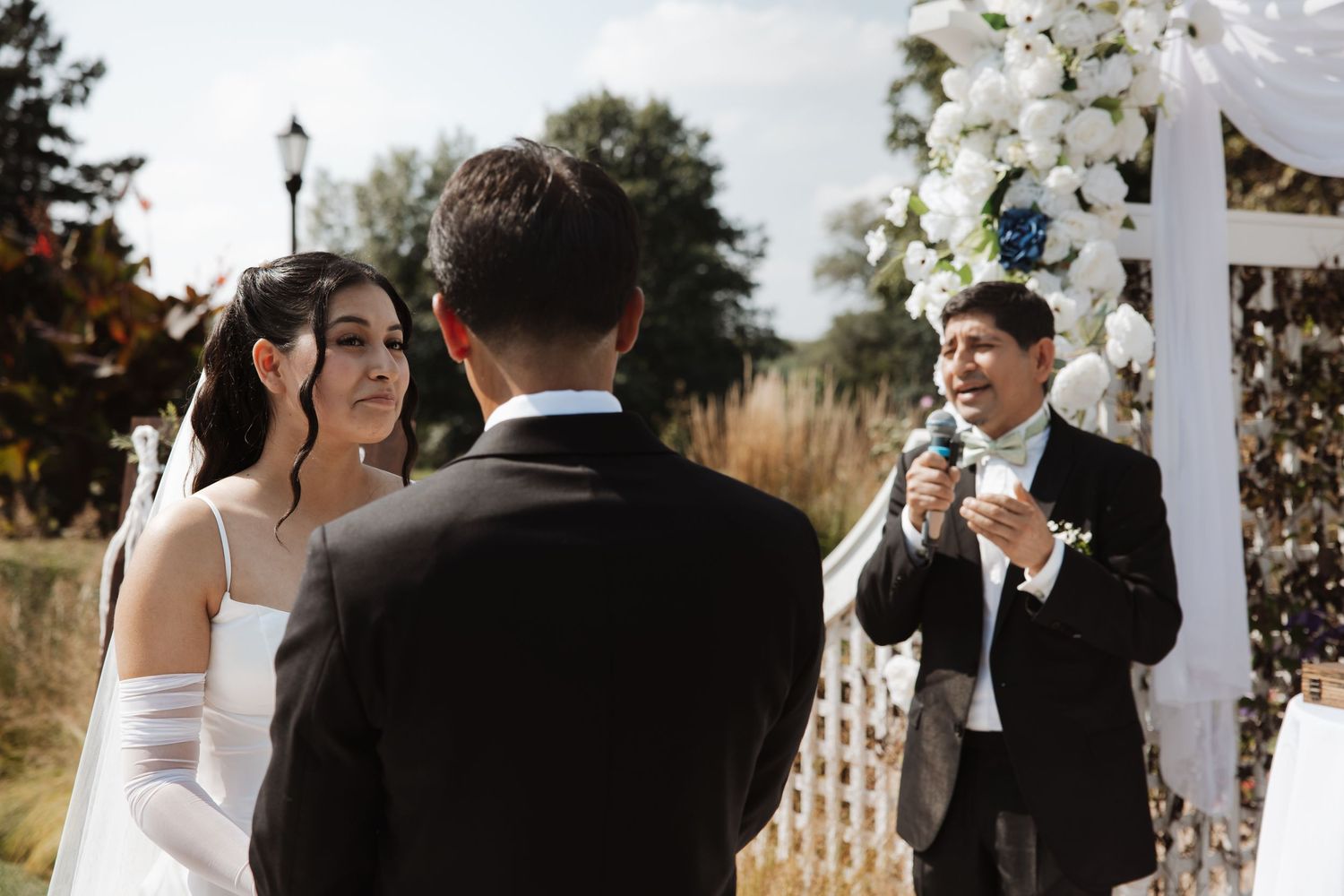 Bride and groom exchange vows at outdoor wedding ceremony with officiant speaking at floral arch.