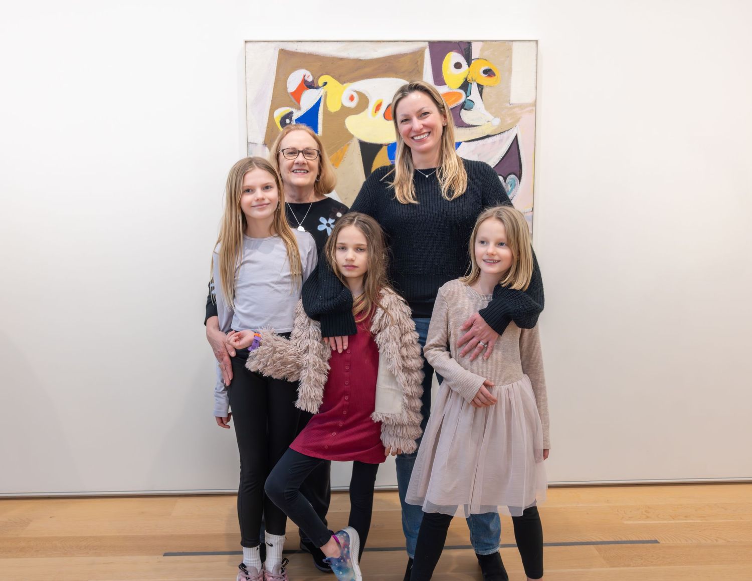 Two women and three girls smiling together in front of colorful abstract museum artwork.