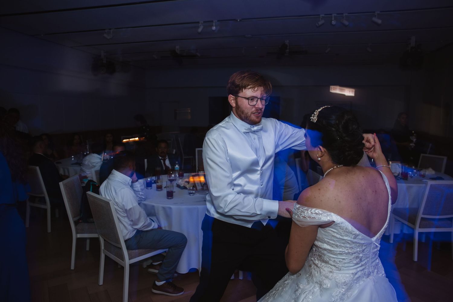 Groom in white shirt dancing with bride in off-shoulder wedding gown at reception.