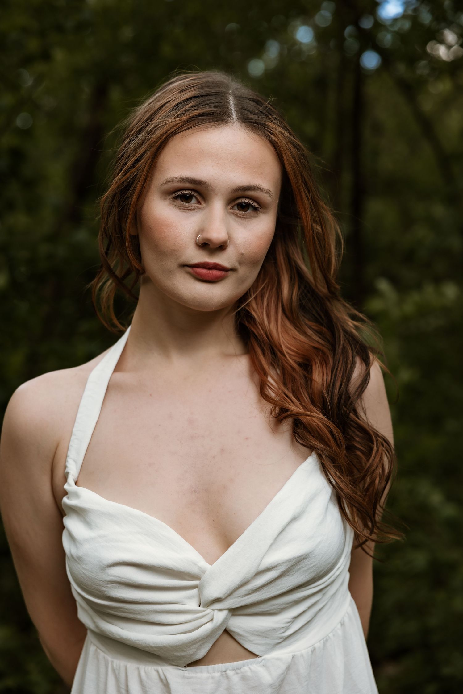 Close portrait of young woman with auburn hair in white halter dress in forest.
