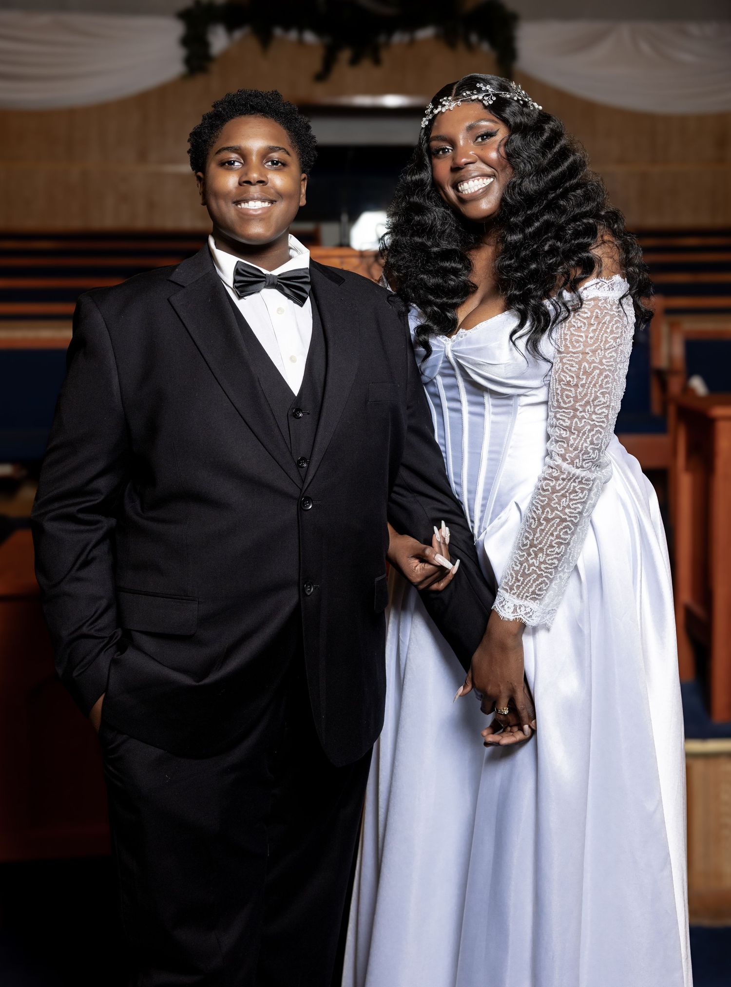 Young man in black tuxedo and woman in white bridal gown posing together in a church.