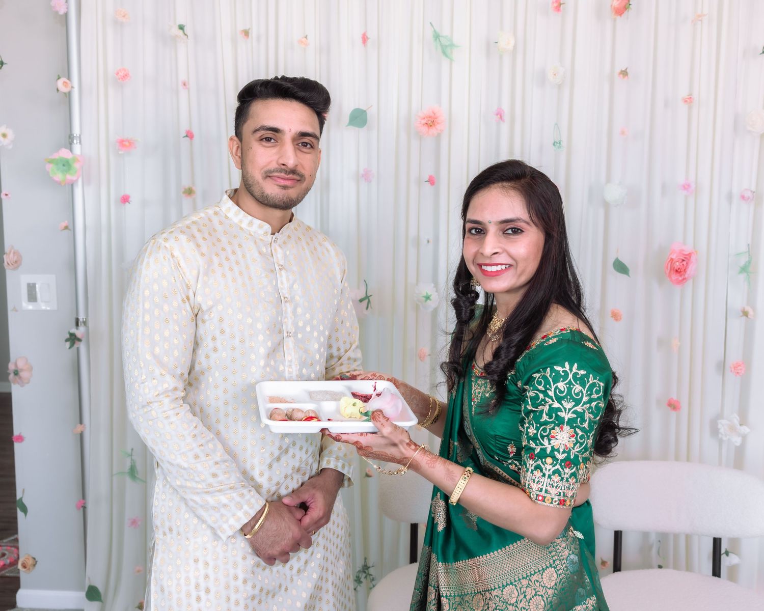 South Asian couple in traditional Indian attire holding sweet box at festive celebration.