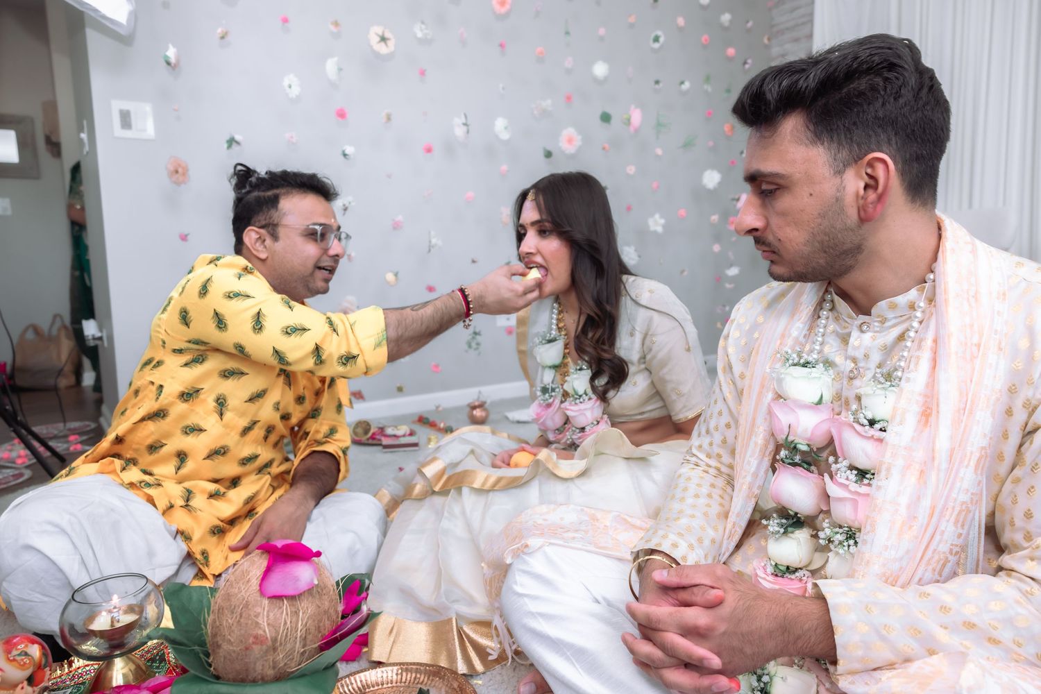 Hindu wedding priest in yellow kurta performing ritual offering to bride and groom during Indian ceremony.