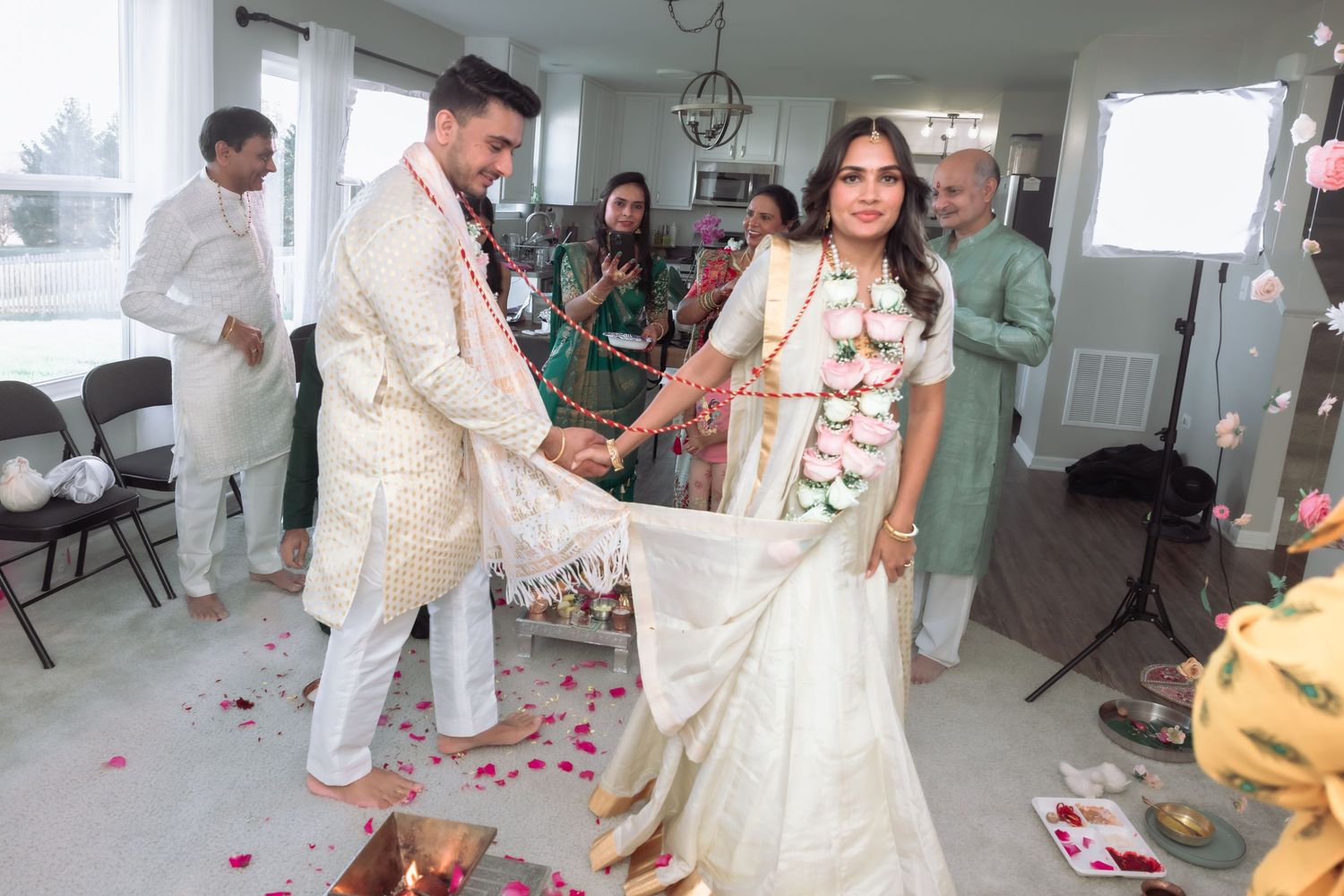 Bride and groom walk together through a flower petal-strewn aisle at an Indian wedding.