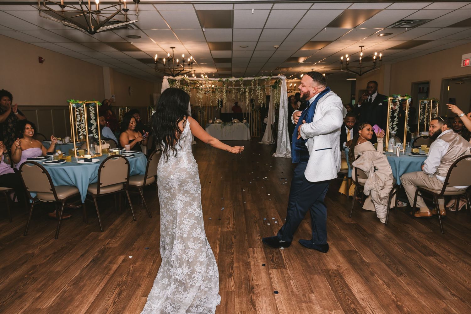Bride in lace gown and groom in white jacket sharing first dance at wedding reception.