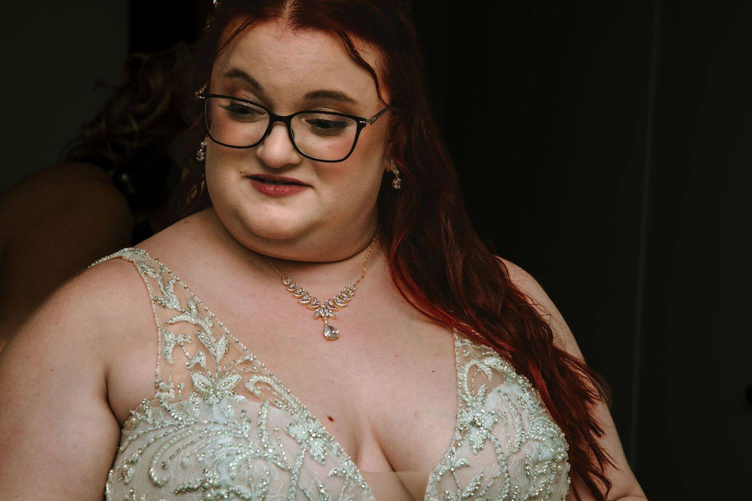 Bride with red hair and glasses wearing a beaded green and white wedding gown.