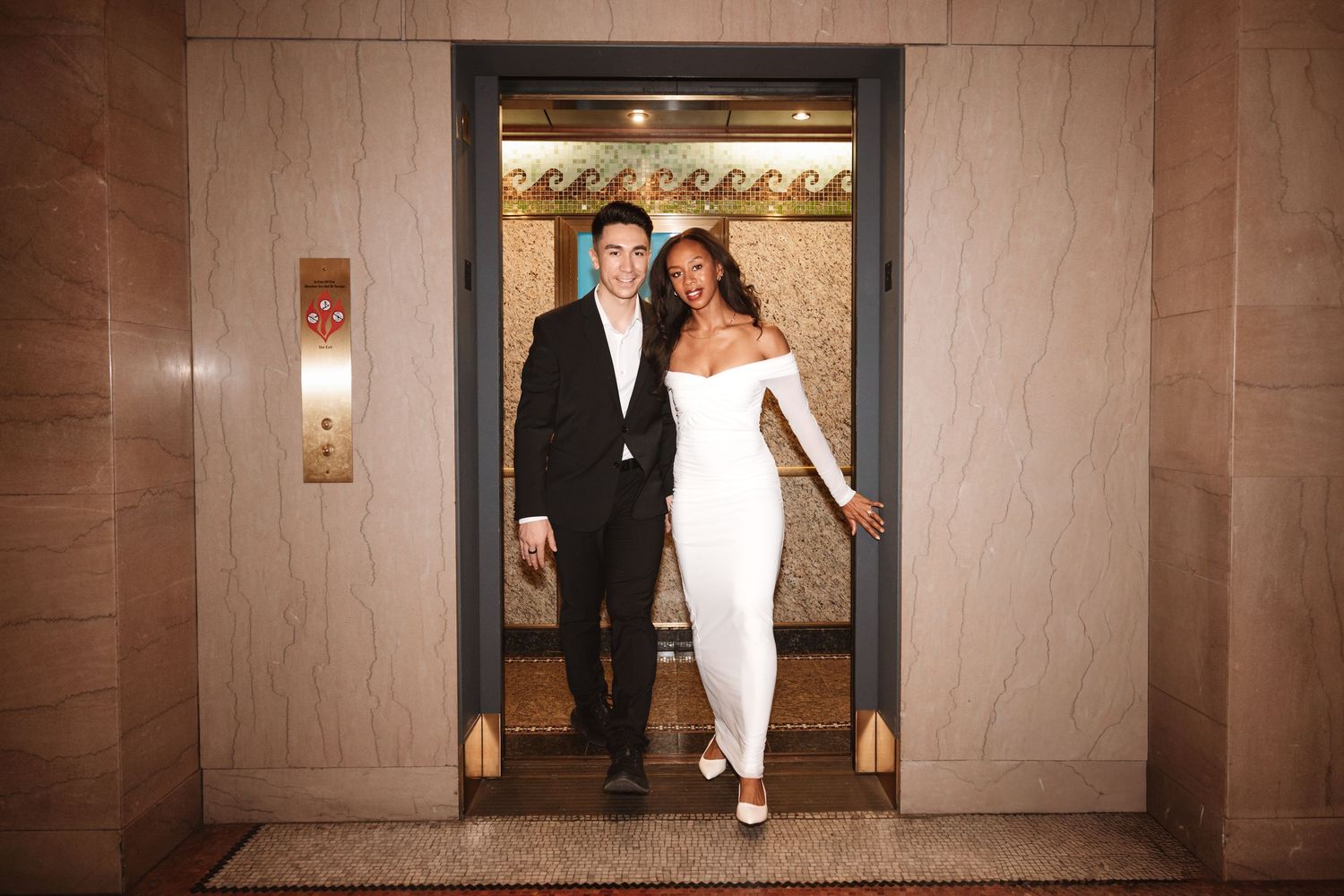 Happy couple posing in elevator doorway, groom in black suit and bride in white off-shoulder dress.Chicago Wedding Photographer