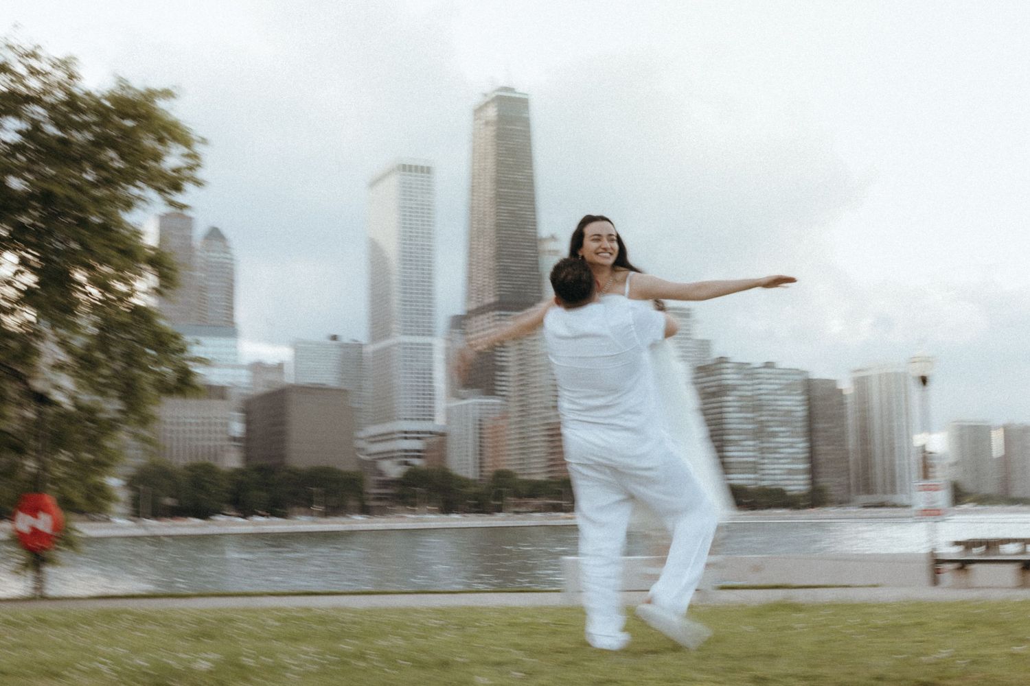 Woman in white outfit dancing joyfully in a park with a city skyline and river in the background.