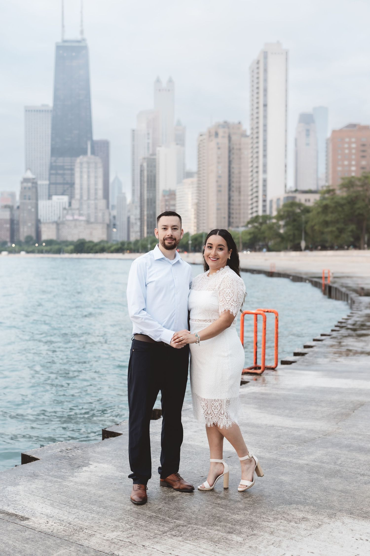 Couple in white outfits posing on Chicago lakefront with city skyline backdrop.