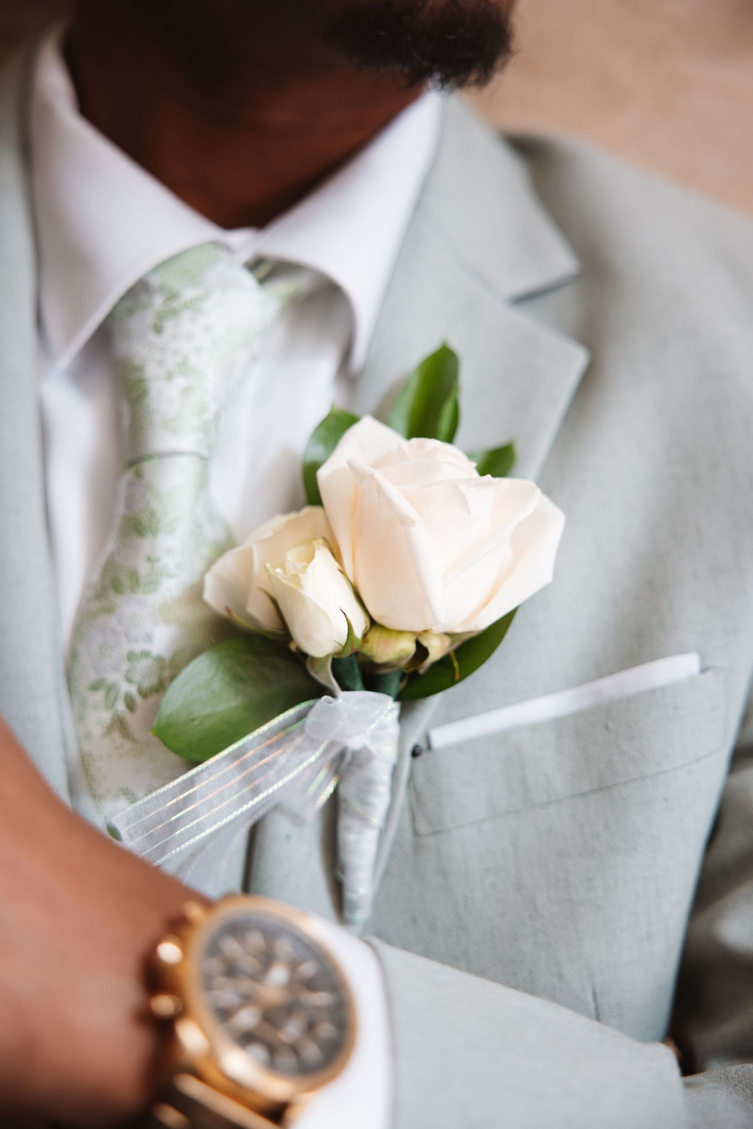 Groom in light gray suit with white rose boutonniere and gold watch at wedding.