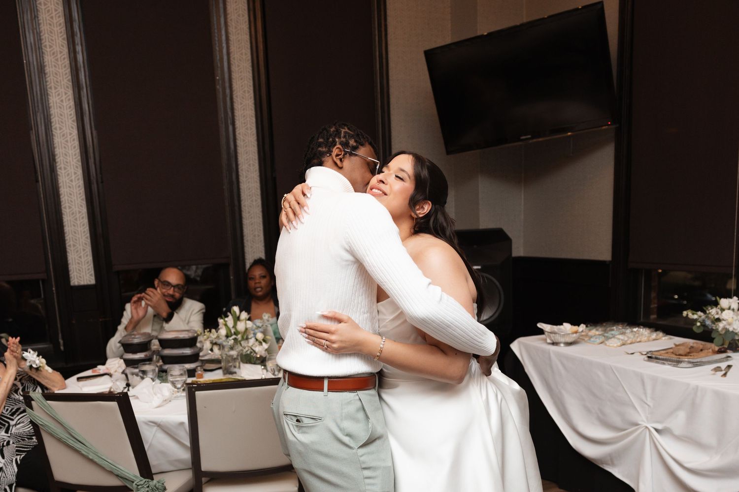 Bride in strapless gown embraces groom in white outfit during wedding reception dance.