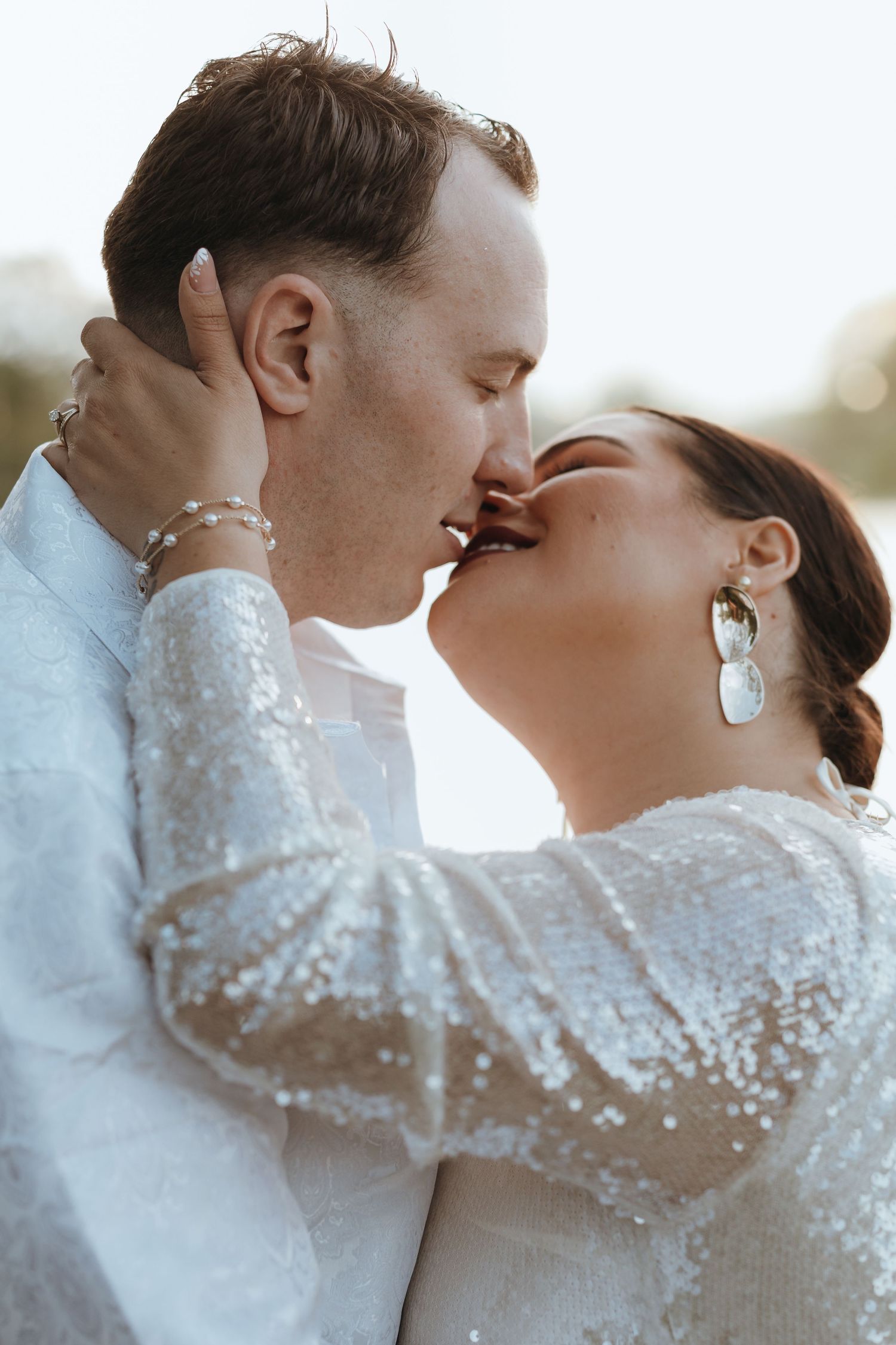 Bride and groom sharing a tender kiss outdoors in soft natural light on their wedding day.