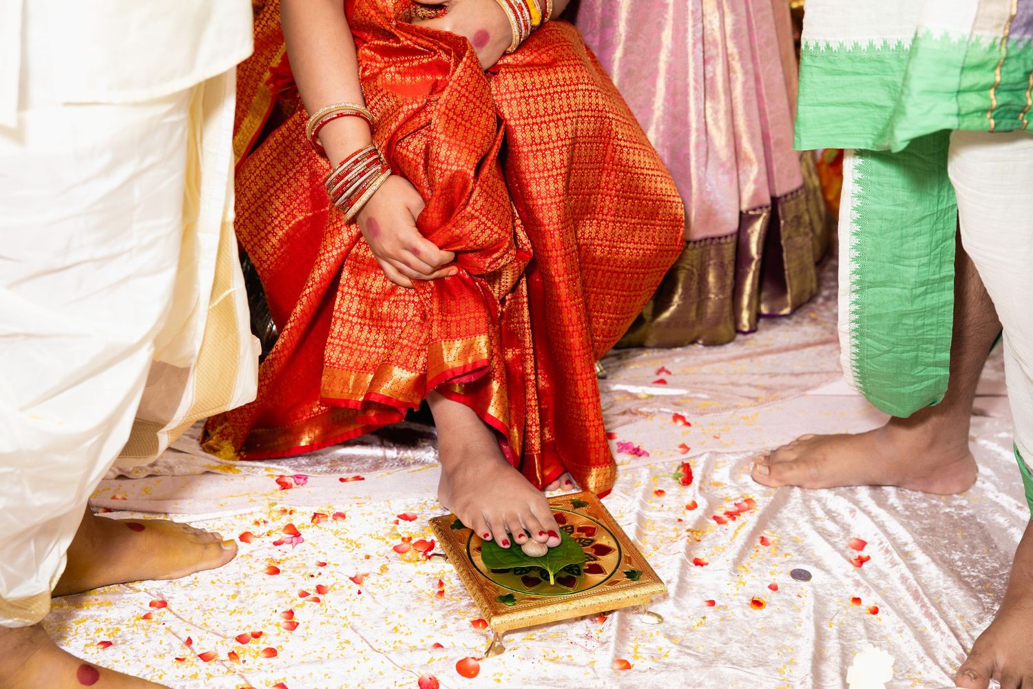 Close-up of Indian bride in red saree performing traditional wedding ritual with flower petals.
