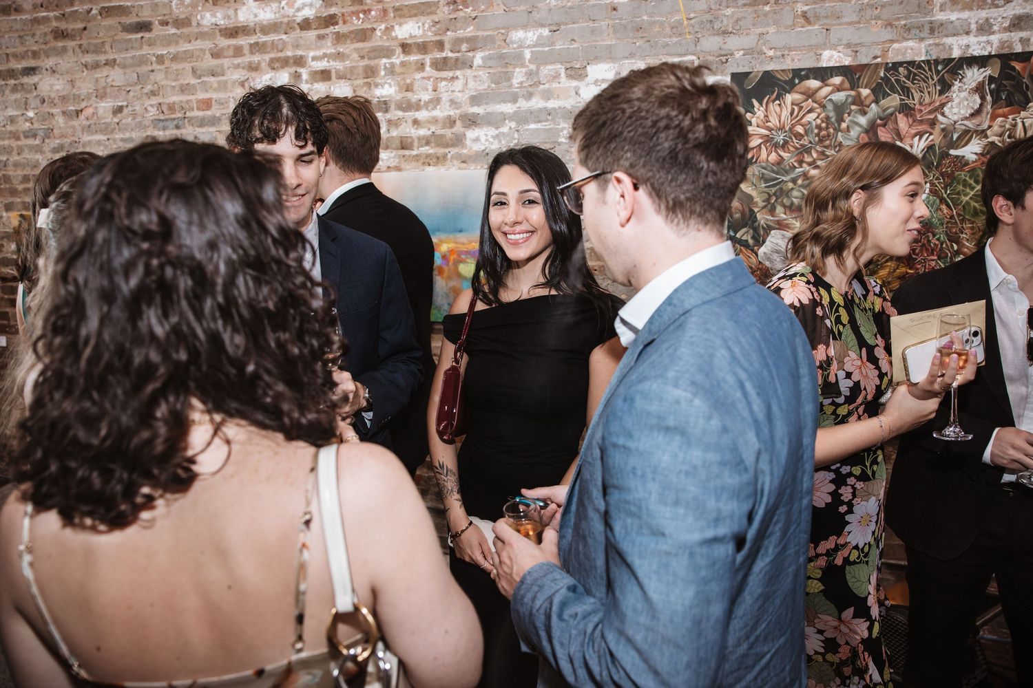 Guests mingling and smiling at an art gallery social event with brick walls.