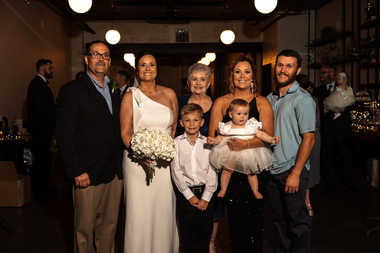 Smiling family group poses with bride and her white floral bouquet at reception.